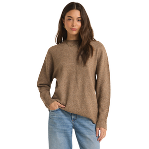 Woman in a brown turtleneck sweater and blue jeans.