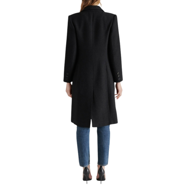 Woman from behind wearing a long black coat, blue jeans, and black heels.